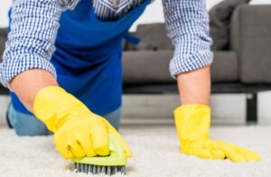 Hombre con delantal y guantes limpiando una alfombra, ofreciendo servicio premium de lavado en Bucaramanga.