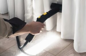 Persona limpiando una cortina con una aspiradora en Cartagena, servicio de limpieza a domicilio.