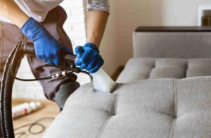Persona limpiando un sofá con una aspiradora en Bucaramanga, mostrando un servicio de limpieza profesional de muebles.