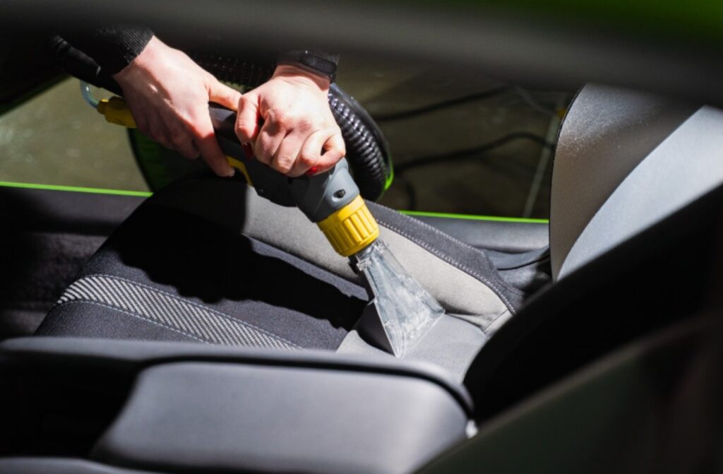 Persona aspirando el asiento de un auto durante un servicio de lavado interior en Cartagena. Higiene total garantizada