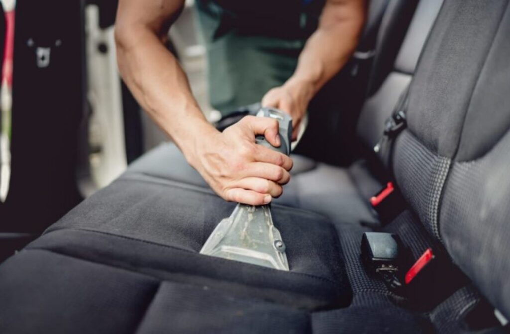 Persona limpiando el asiento de un auto con una aspiradora en un servicio de lavado interior en Pereira.